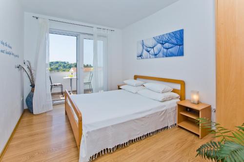 a white bedroom with a bed and a window at HVAR apartments 8 min to the beach in Hvar