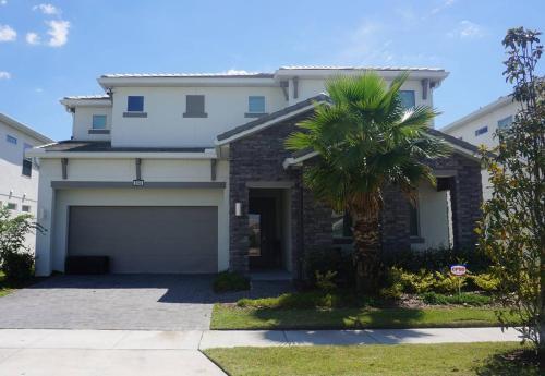 a white house with a garage and a palm tree at 3840 Supreme Villa 6Bd Private Pool and Game Room in Kissimmee
