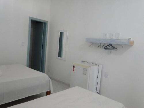 a white room with two beds and a refrigerator at Pousada Vila Mar in Itaúnas
