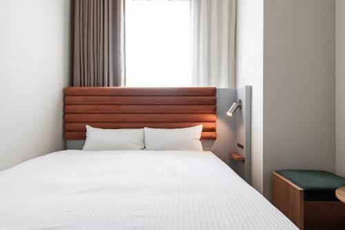 a bedroom with a white bed with a wooden headboard at KIRO Hiroshima by THE SHARE HOTELS in Hiroshima