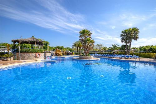 a large blue swimming pool with chairs and palm trees at Camping La Masia in Blanes