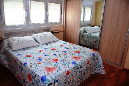 a bedroom with a bed with a floral comforter and a mirror at O Mencer do Camiño in Cee