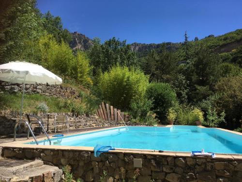 a swimming pool in a stone wall with an umbrella at Les SenS de l'Escalette in Pégairolles-de-lʼEscalette