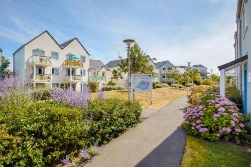 uma passarela em frente a casas com flores em Pierre & Vacances Résidence Le Chant des Oiseaux em Courseulles-sur-Mer