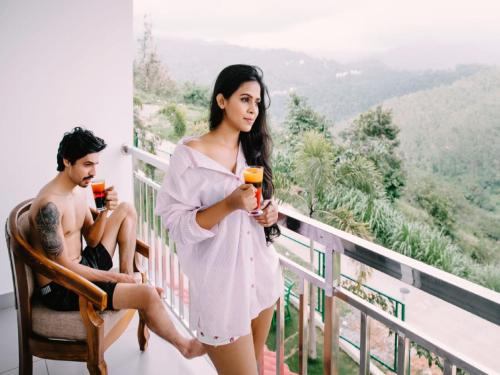 a man and a woman standing on a balcony with drinks at The Lake View Munnar in Munnar