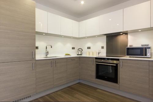 a large kitchen with wooden cabinets and a microwave at Citystay Living - Mill Park Apartments in Cambridge