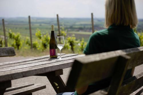 une femme assise sur un banc avec une bouteille de vin dans l'établissement Weingut Schilling, à Seinsheim