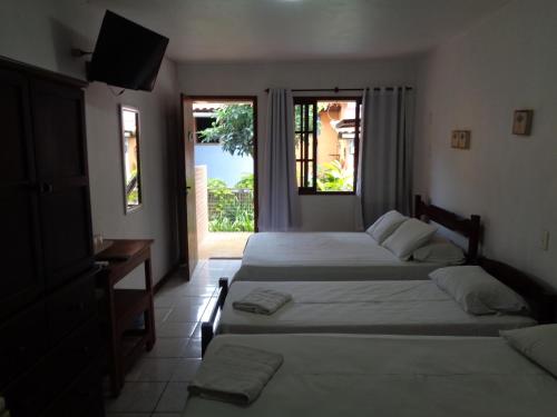 a bedroom with two beds and a desk and a window at Pousada Barcarola in Búzios
