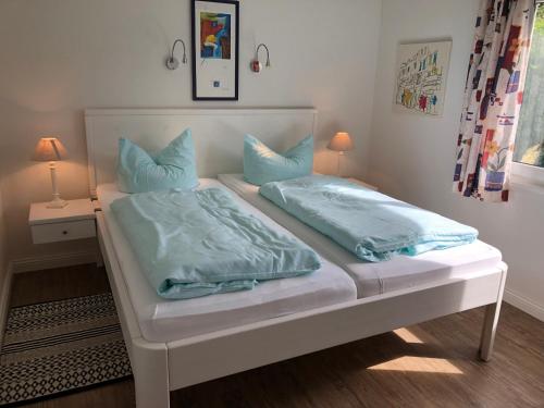 ein weißes Bett mit blauen Kissen darüber in der Unterkunft Bungalow 3 in Wyk auf Föhr
