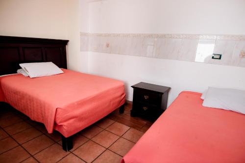 two beds in a room with red sheets and a table at Hotel María Elena in Durango