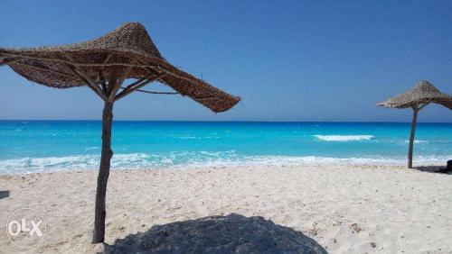 two straw umbrellas on a beach with the ocean at شاليه عايدة بيتش للعائلات فقط in El Alamein