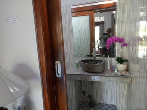 a bathroom with a sink and a person in a mirror at Suryadina Guest House in Ubud