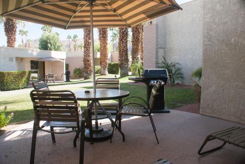 a table and chairs with an umbrella and a grill at Desert Isle Resort, a VRI resort in Palm Springs