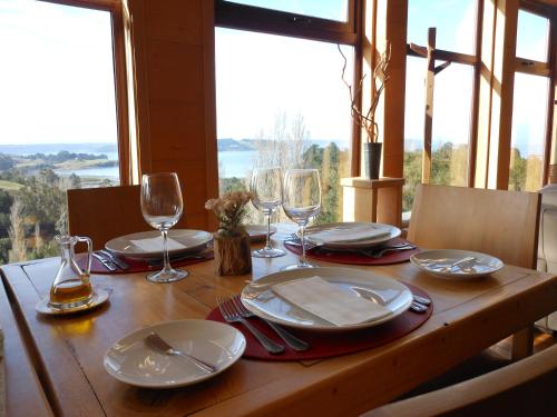 a wooden table with plates and wine glasses on it at Hotel Parque Quilquico in Castro
