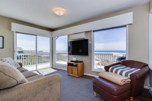 a living room with a couch and a tv and windows at Spindrift Oceanfront Home - The Helm in Bandon