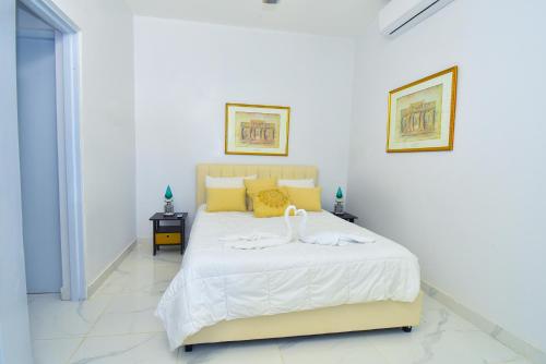 a white bedroom with a large bed with yellow pillows at Rosil Place in San Felipe de Puerto Plata