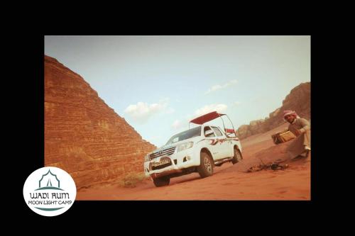 a man standing next to a white truck on a dirt road at Wadi Rum Moon Light Camp in Wadi Rum