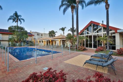 a resort with a swimming pool with chairs and palm trees at Mildura Inlander Resort in Mildura
