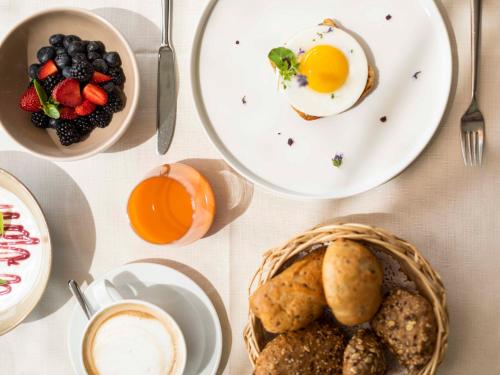 a table with plates of breakfast food and a basket of bread at Biohotel theiner's garten in Lana