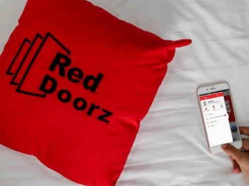 a person holding a red pillow and a cell phone on a bed at RedDoorz @ Galuh Mas in Karawang