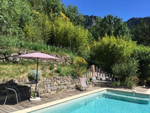 uma piscina com cadeiras e um guarda-sol ao lado de um quintal em Les SenS de l'Escalette em Pégairolles-de-lʼEscalette