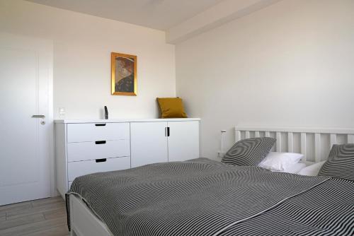 a white bedroom with a bed and a dresser at Weiße Düne Ferienwohnung *Weiße Düne 9 / Gen Norden* in Wittdün