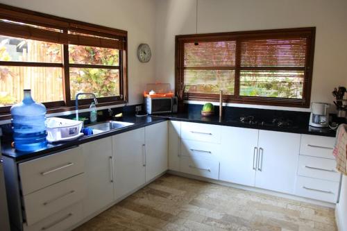 eine Küche mit weißen Schränken, einem Waschbecken und 2 Fenstern in der Unterkunft Villa Cantik in Lovina