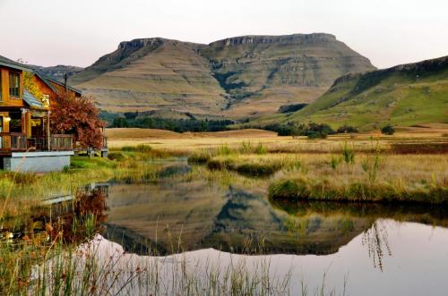 a house next to a lake with mountains in the background at Sani Valley Nature Lodges in Himeville