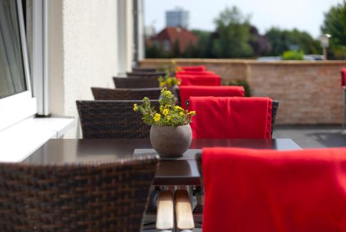 a row of tables with red chairs and a vase with flowers at Tryp by Wyndham Luebeck Aquamarin in Lübeck