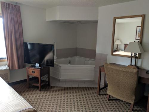 Habitación de hotel con bañera, TV y dormitorio. en Boarders Inn and Suites by Cobblestone Hotels - Ripon, en Ripon