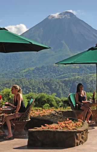 two women sitting at tables with a mountain in the background at The Springs Resort & Spa at Arenal in Fortuna