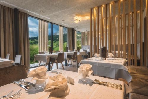 un restaurante con mesas y sillas blancas y ventanas grandes en Hotel Lech Da Sompunt, en Badia