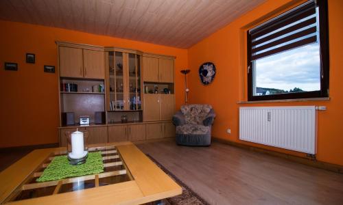 ein Wohnzimmer mit orangefarbenen Wänden, einem Tisch und einem Fenster in der Unterkunft am Balkon des Erzgebirges in Bernsbach
