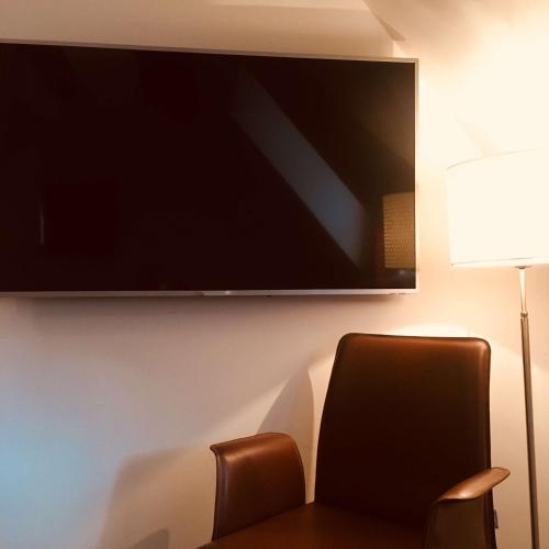 a flat screen tv hanging on a wall with a chair at Hotel KLE, BW Signature Collection in Kaysersberg