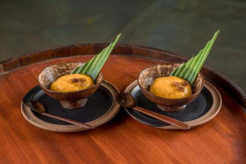 two bowls of food on a wooden table with spoons at Amethyst Resort Passikudah in Pasikuda