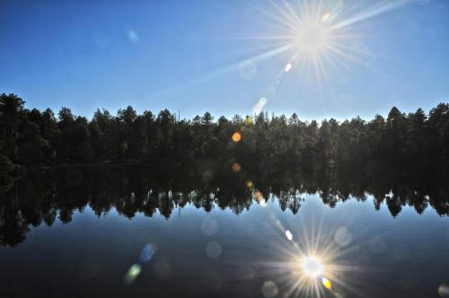 a reflection of the sun on a lake with trees at Horský apartmán Zvonička in Rejvíz
