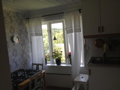 a kitchen with a window with white curtains and a table at Annies Hus in Årjäng