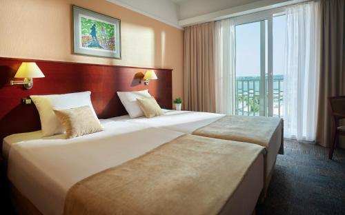 Grand Hotel Portoroz 4* superior – Terme & Wellness LifeClass في بوروتوروج: سريرين في غرفة الفندق مع نافذة كبيرة