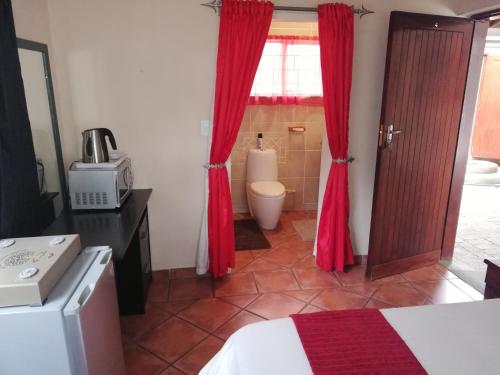 a bedroom with red curtains and a bathroom with a toilet at 52 Oaks Guest House in Sasolburg