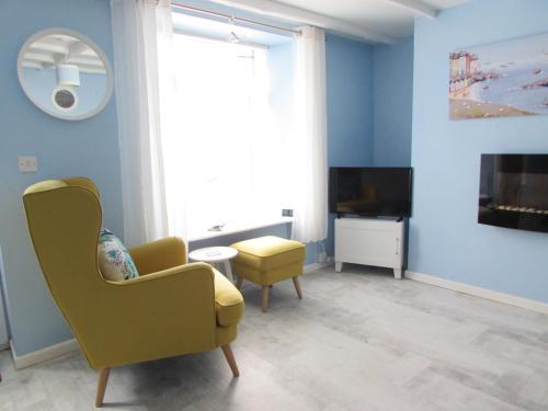 a living room with a yellow chair and a tv at The Cuddy - Apartment with garden in Brixham