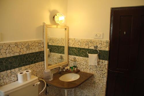 een badkamer met een wastafel, een spiegel en een toilet bij WelcomHeritage Panjim Pousada in Panaji
