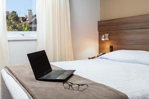 a laptop computer sitting on a bed with a pair of glasses at Hotel Fioreze Centro in Gramado