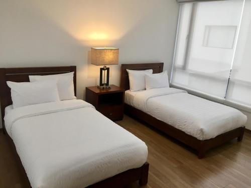 1 Schlafzimmer mit 2 Betten, einer Lampe und einem Fenster in der Unterkunft Foresta Boutique Apartments in Quito