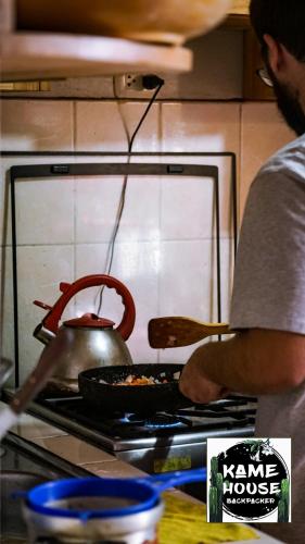 a man cooking food on a stove with a tea kettle at Kame House hostel in Huaraz