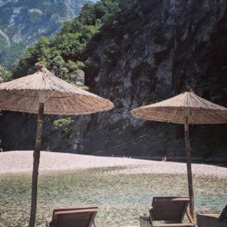 two straw umbrellas and chairs on a beach at Park Blini Shala River in Mollʼ e Shoshit