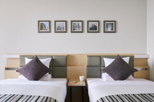 two beds in a hotel room with three pictures on the wall at Art Hotel Osaka Bay Tower in Osaka