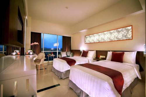 a hotel room with two beds and a desk at Atria Hotel Malang in Malang