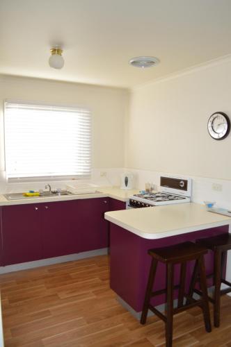 uma cozinha com armários roxos, um lavatório e uma janela em Waterfall Cottage em Rosebud