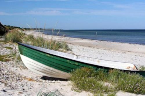 a green and white boat sitting on the beach at Holldiay house near the beach in Yderby