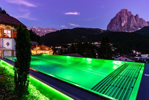 a green swimming pool with mountains in the background at Garni Residence Soraiser in Selva di Val Gardena